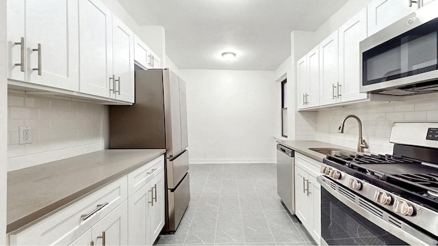 kitchen with baseboards, white cabinetry, a sink, appliances with stainless steel finishes, and backsplash