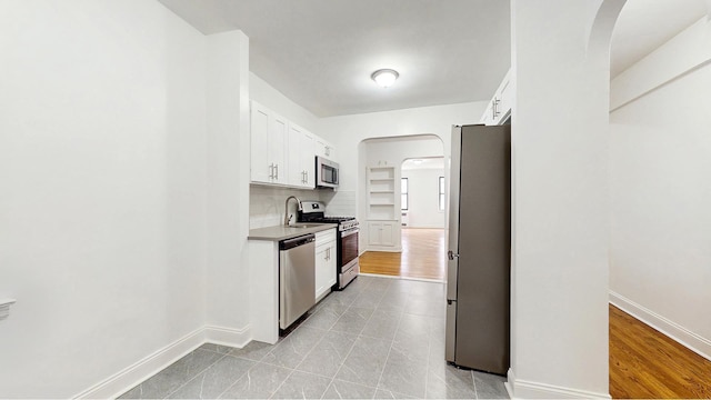 kitchen featuring baseboards, arched walkways, white cabinetry, and appliances with stainless steel finishes