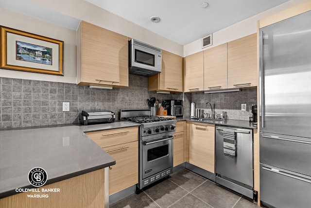 kitchen featuring visible vents, a sink, light brown cabinetry, and high end appliances