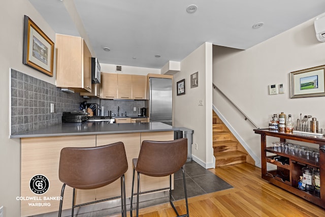 kitchen featuring a kitchen bar, a peninsula, high end fridge, wood finished floors, and backsplash