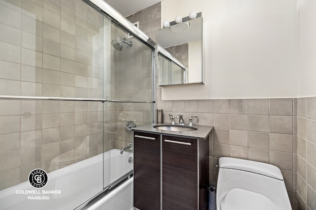 bathroom featuring shower / bath combination with glass door, vanity, tile walls, and toilet
