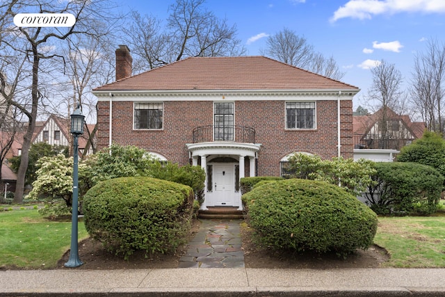 colonial inspired home with brick siding, a chimney, a tile roof, and a front lawn