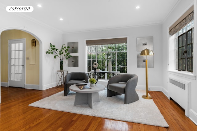 living area with visible vents, ornamental molding, radiator, hardwood / wood-style floors, and arched walkways