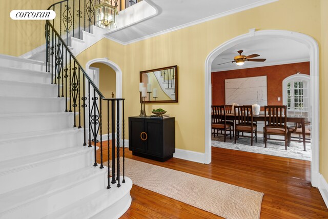 entrance foyer featuring a ceiling fan, ornamental molding, wood finished floors, stairway, and arched walkways