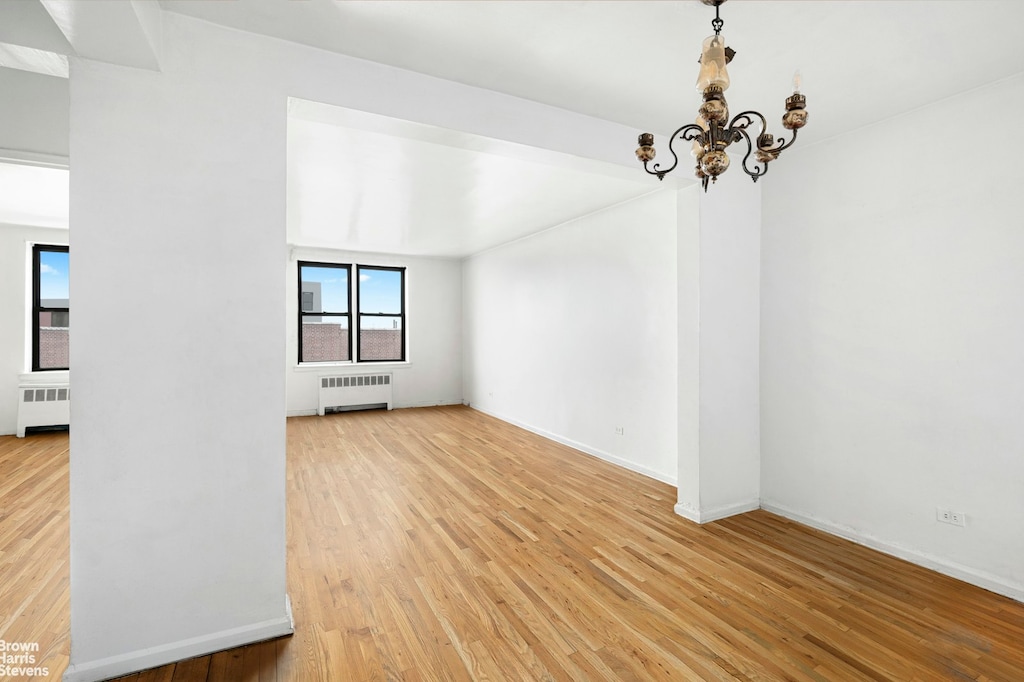 empty room featuring light wood-style floors, radiator, baseboards, and a chandelier