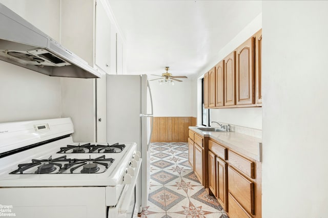 kitchen featuring ceiling fan, a sink, a wainscoted wall, white gas range, and under cabinet range hood