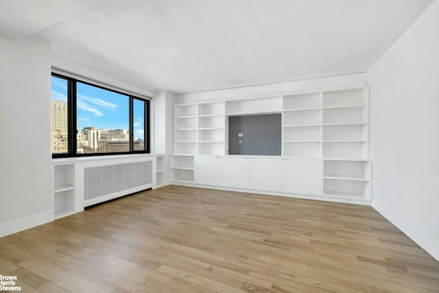 420 E 64th St Unit W12Fg, New York City, NY 10065 - unfurnished living room featuring radiator heating unit, wood finished floors, and built in shelves
