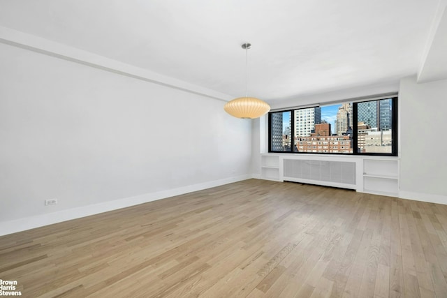 spare room featuring radiator heating unit, light wood finished floors, and baseboards