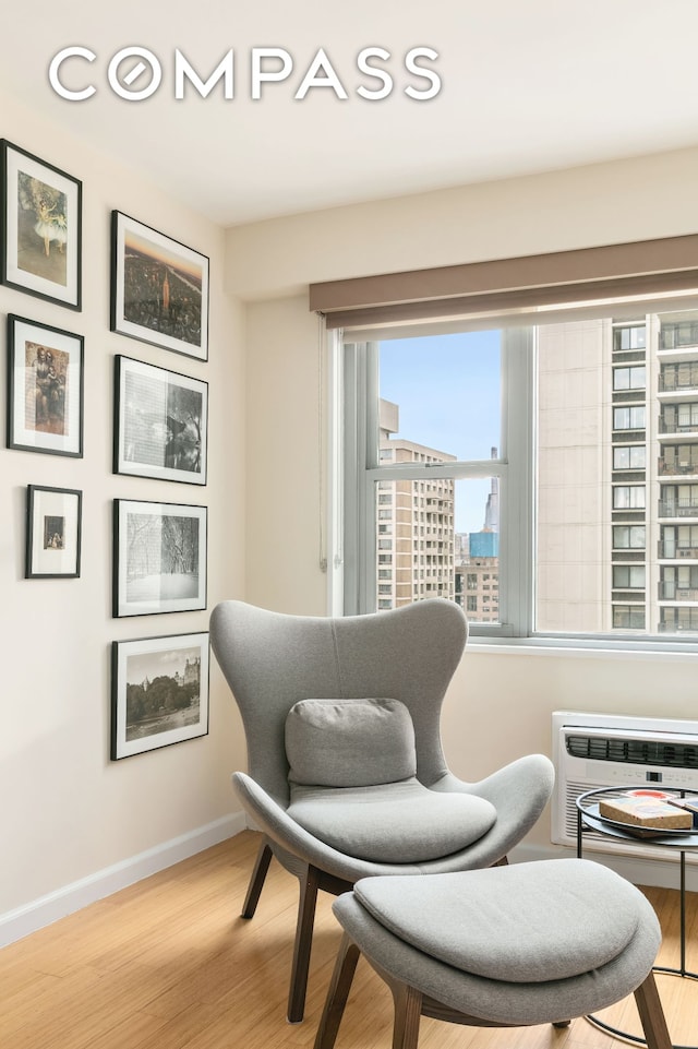 living area featuring a wall mounted air conditioner, a city view, wood finished floors, and baseboards