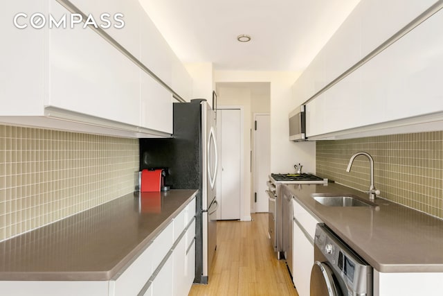 kitchen featuring white cabinetry, light wood-style flooring, a sink, appliances with stainless steel finishes, and washer / dryer