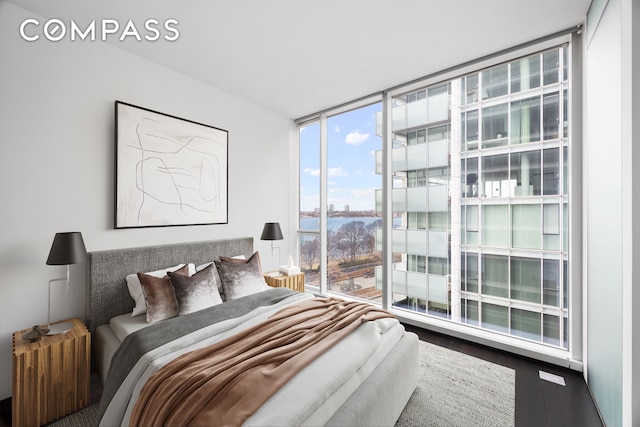 bedroom with a water view, expansive windows, and wood finished floors