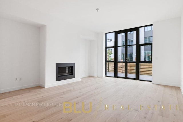 123 King St, New York City, NY 11231 - unfurnished living room featuring wood finished floors, a glass covered fireplace, baseboards, and floor to ceiling windows