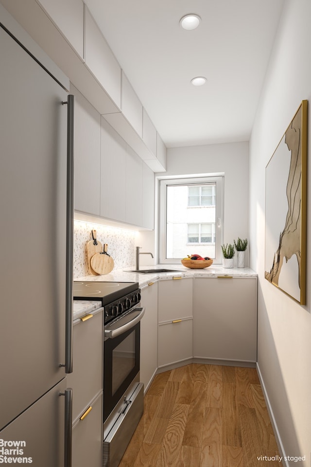 kitchen with a sink, appliances with stainless steel finishes, white cabinets, light countertops, and light wood-style floors