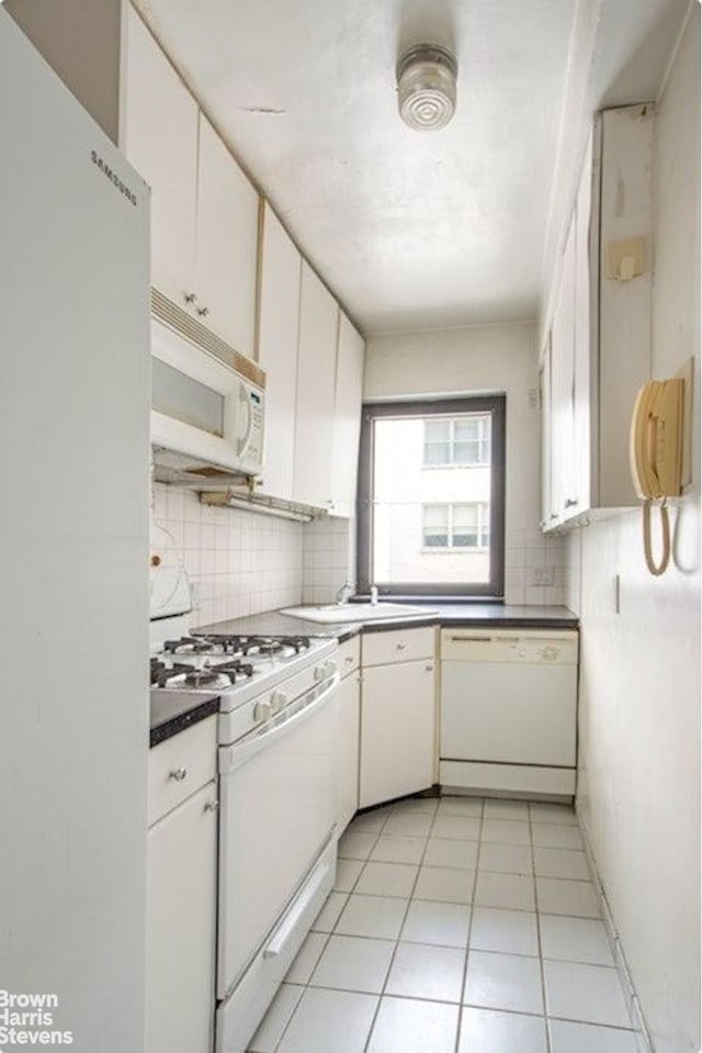 kitchen featuring light tile patterned floors, white appliances, a sink, white cabinets, and tasteful backsplash