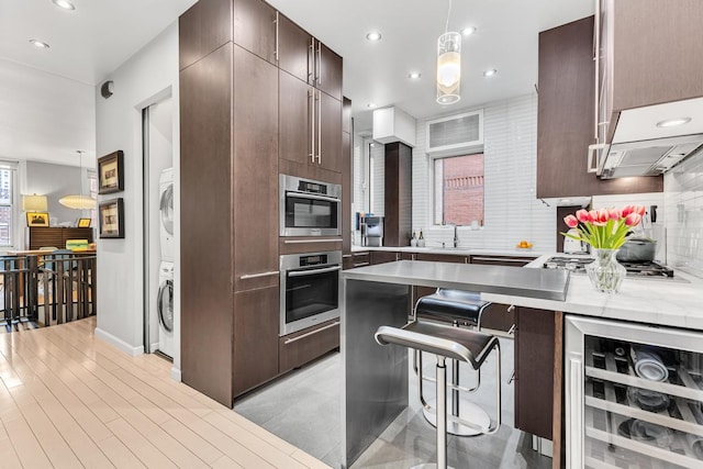 kitchen featuring stacked washer and dryer, a kitchen bar, light countertops, wine cooler, and stainless steel appliances