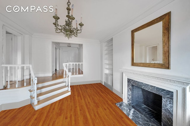 unfurnished living room with ornamental molding, light wood-style floors, baseboards, built in shelves, and a notable chandelier