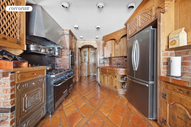 243 E 61st St, New York City, NY 10065 - kitchen featuring appliances with stainless steel finishes, wall chimney range hood, tile patterned flooring, and brick wall