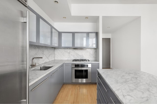 210 Lafayette St Unit 5B, New York City, NY 10012 - kitchen with stainless steel appliances, a sink, gray cabinetry, backsplash, and light wood finished floors