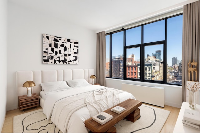 210 Lafayette St Unit 5B, New York City, NY 10012 - bedroom featuring radiator heating unit, a city view, wood finished floors, and baseboards