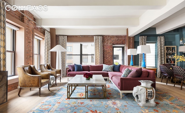living room with wood finished floors, a healthy amount of sunlight, beam ceiling, and brick wall