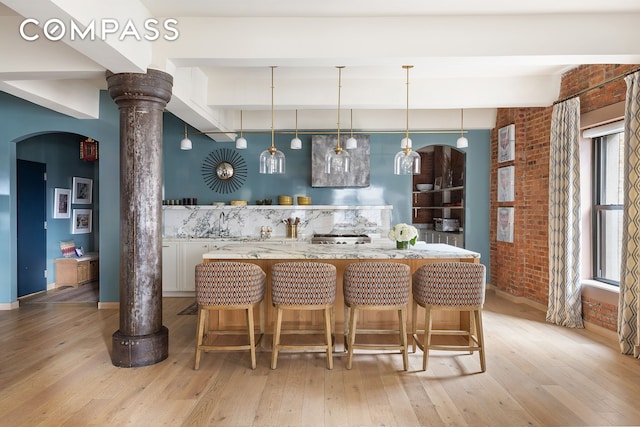 bar featuring brick wall, arched walkways, light wood-style floors, and hanging light fixtures