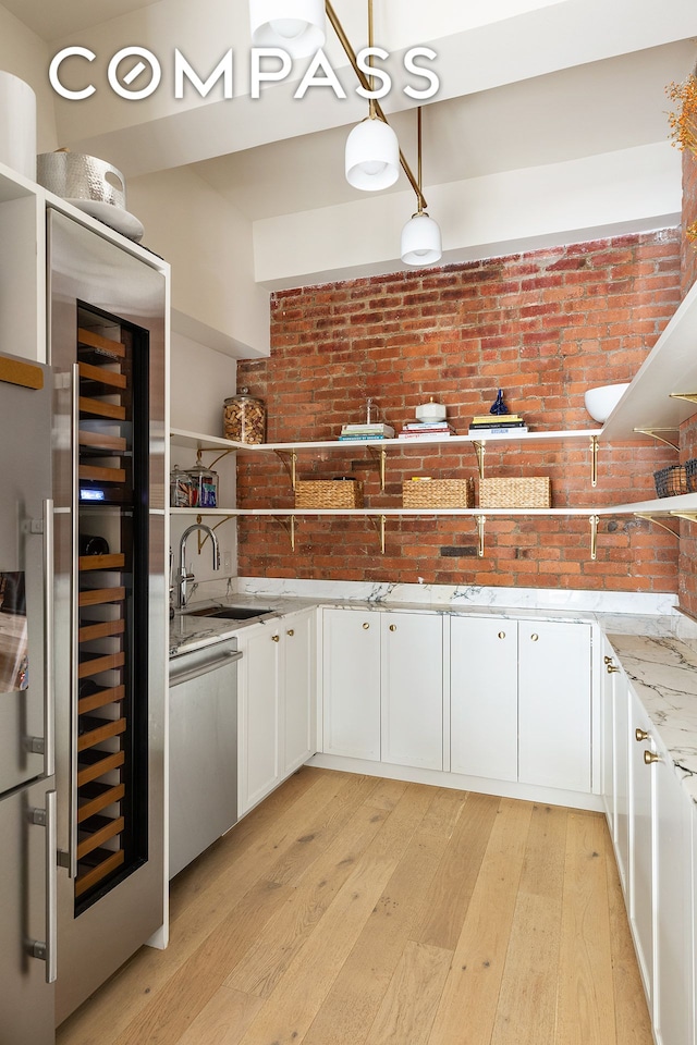 kitchen featuring stainless steel dishwasher, a sink, beverage cooler, light wood-type flooring, and brick wall