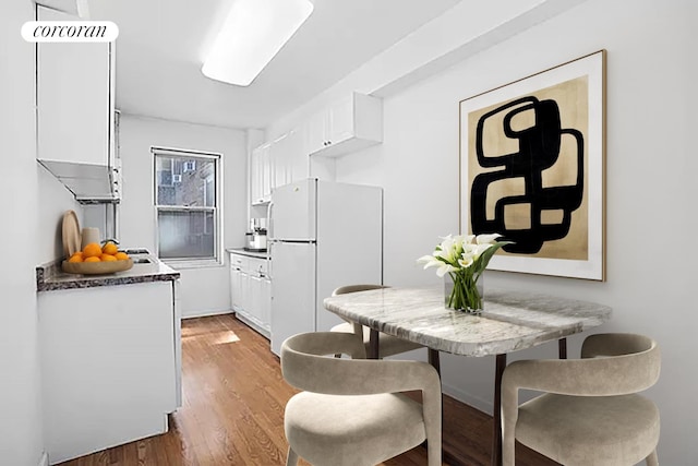 kitchen featuring freestanding refrigerator, white cabinets, light wood-type flooring, and dark countertops