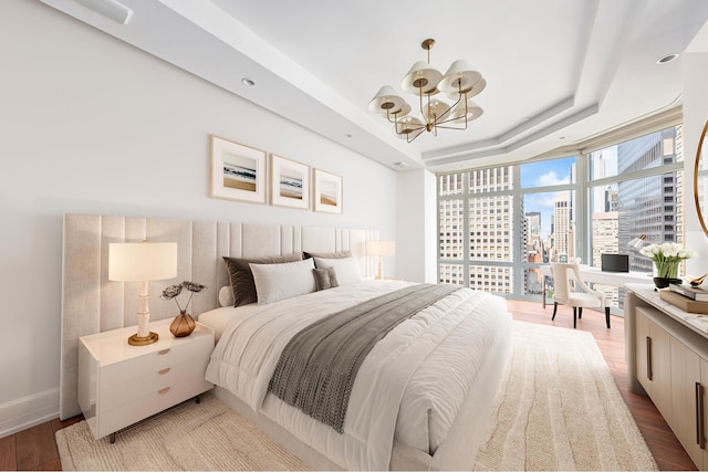 bedroom featuring baseboards, an inviting chandelier, wood finished floors, a view of city, and a raised ceiling