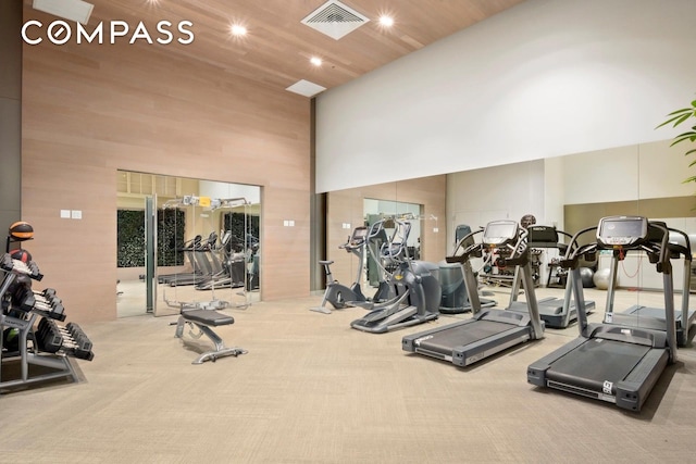 exercise room with visible vents, carpet flooring, and a towering ceiling