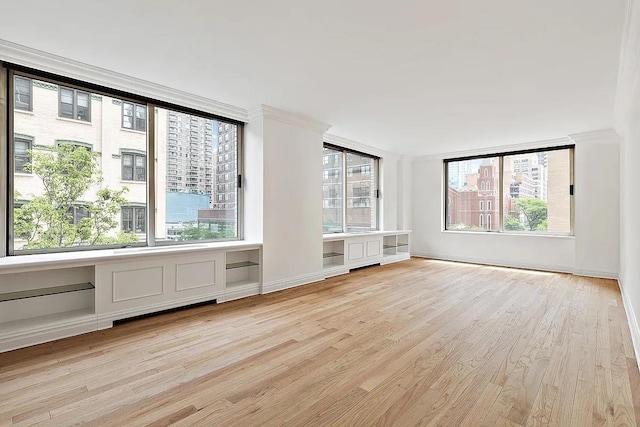 empty room with light wood-type flooring, baseboards, and crown molding