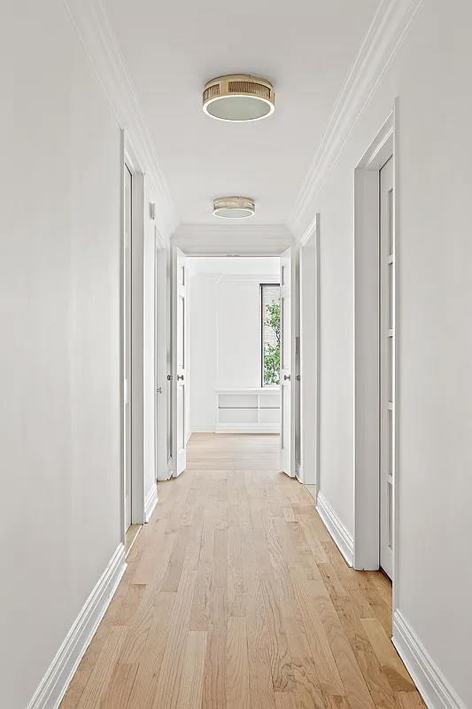 hallway with ornamental molding, light wood-style flooring, and baseboards