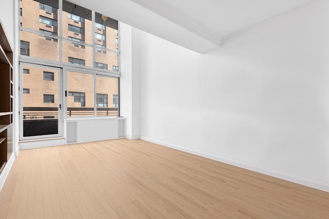 empty room featuring wood finished floors, healthy amount of natural light, ornamental molding, and baseboards