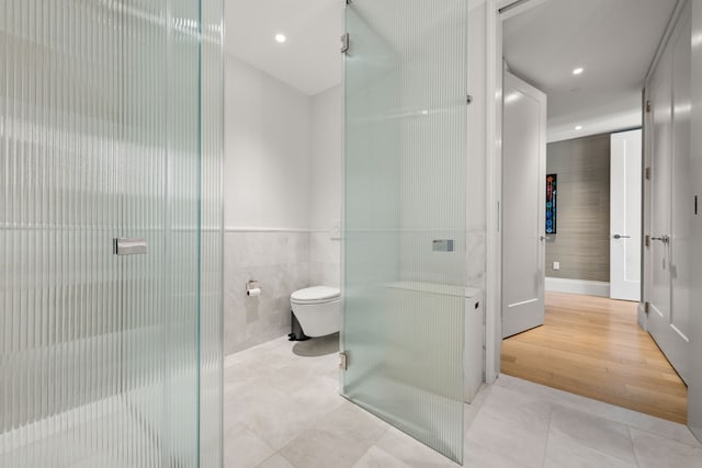 bathroom with tile walls, tile patterned flooring, toilet, a stall shower, and recessed lighting