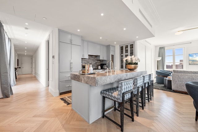 kitchen with gray cabinetry, a breakfast bar area, light stone counters, a sink, and tasteful backsplash