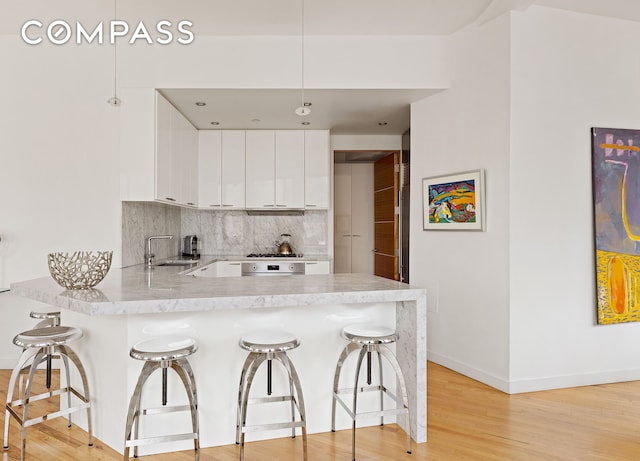 kitchen featuring a peninsula, white cabinetry, backsplash, a kitchen bar, and baseboards