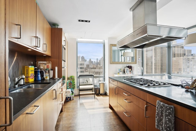 kitchen featuring stainless steel gas stovetop, a city view, dark countertops, island range hood, and a sink