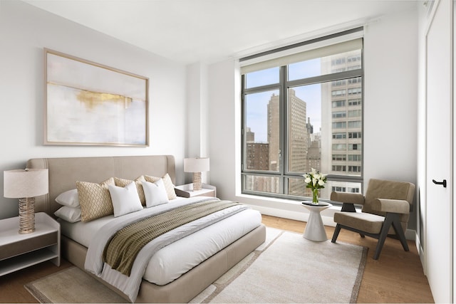 bedroom with wood finished floors, a city view, and expansive windows