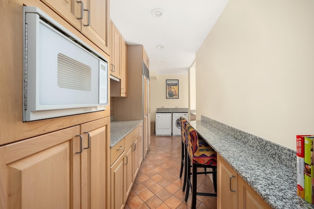875 5th Ave Unit 12Ef, New York City, NY 10065 - kitchen with white microwave, washing machine and clothes dryer, light brown cabinetry, recessed lighting, and light stone counters