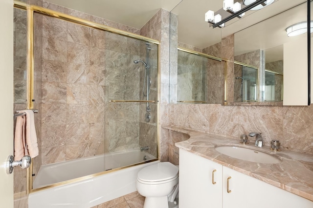 bathroom featuring vanity, combined bath / shower with glass door, toilet, and tile walls