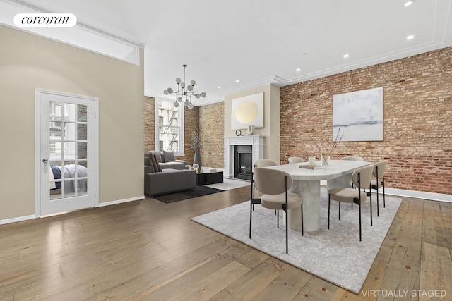 dining area with brick wall, a wealth of natural light, a glass covered fireplace, and hardwood / wood-style floors