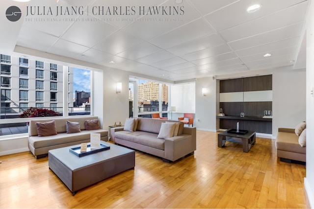 living area with light wood-type flooring, a paneled ceiling, recessed lighting, and baseboards