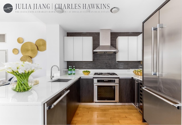 kitchen with a sink, stainless steel appliances, modern cabinets, and wall chimney exhaust hood