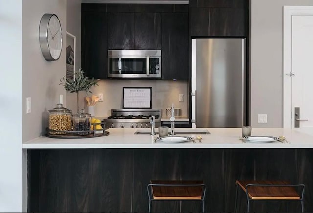 kitchen with modern cabinets, a sink, light countertops, appliances with stainless steel finishes, and dark cabinetry