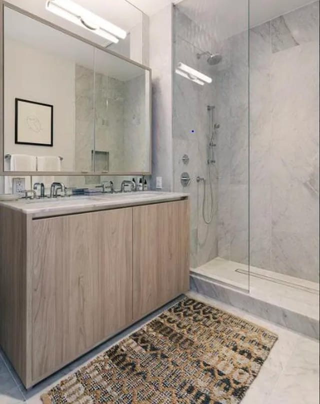 bathroom with marble finish floor, a walk in shower, double vanity, and a sink