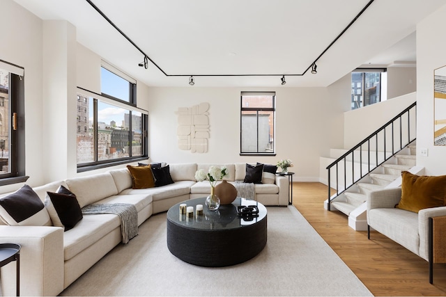 living room with rail lighting, light wood finished floors, and stairway