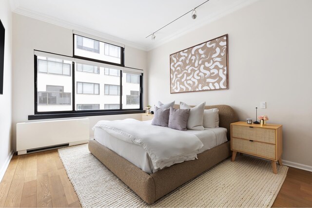 bedroom with radiator, ornamental molding, wood finished floors, track lighting, and baseboards