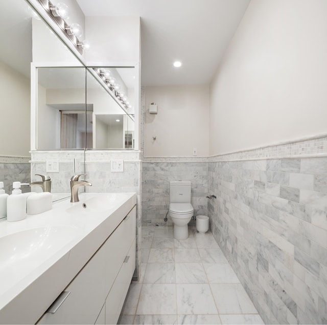 full bath with tile walls, wainscoting, toilet, marble look tile flooring, and double vanity