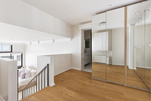 corridor with light wood-type flooring, an upstairs landing, and baseboards