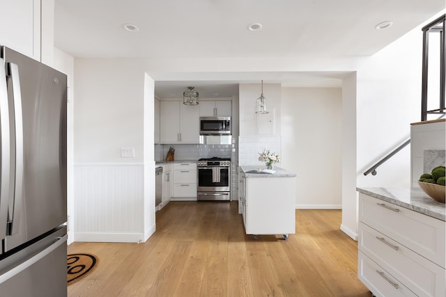 kitchen featuring stainless steel appliances, light wood-type flooring, white cabinetry, decorative backsplash, and light stone counters