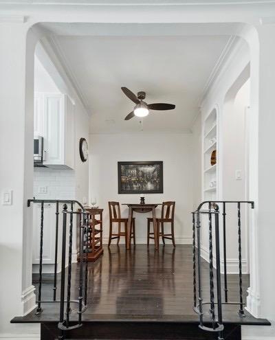 corridor featuring ornamental molding, wood finished floors, arched walkways, and baseboards